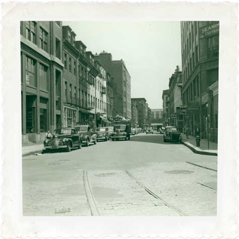 A black and white wide shot of the intersection of Beach Street and Harrison Avenue in Boston, taken in June 1942. Tall buildings line both sides of the street, and cars are parked along one side of the road.