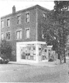 A small brick mixed used building sits on a corner in Cambridge. Few details are visible in the old, grainy photograph.